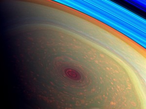 This spectacular, vertigo inducing, false-color image from NASA's Cassini mission highlights the storms at Saturn's north pole. The angry eye of a hurricane-like storm appears dark red while the fast-moving hexagonal jet stream framing it is a yellowish green. Low-lying clouds circling inside the hexagonal feature appear as muted orange color. A second, smaller vortex pops out in teal at the lower right of the image. The rings of Saturn appear in vivid blue at the top right. 