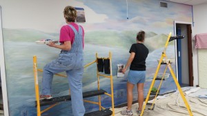 Jan Kostka (l) and Kayde Sberal (r) work on a prairie mural in the Lime Creek Nature Center auditorium.