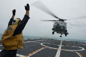U.S. Navy Petty Officer 2nd Class Adam Garnett signals an MH-60R Sea Hawk helicopter from Helicopter Maritime Strike Squadron 35 on the flight deck of the littoral combat ship USS Fort Worth, Jan. 3, 2015. Fort Worth is currently in the Java Sea conducting helicopter search-and-recovery operations with the USS Sampson as part of Indonesian-led efforts to locate downed AirAsia Flight 8501. U.S. Navy photo by Petty Officer 2nd Class Antonio P. Turretto Ramos  